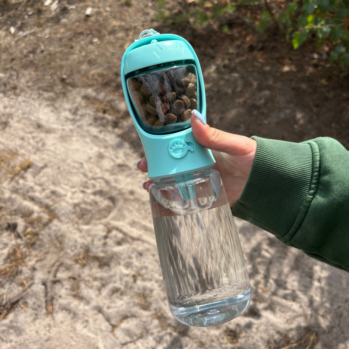 HydraBuddy drinkfles hond mintblauw — hand houdt complete fles buiten vast, snacks zichtbaar door transparant raam