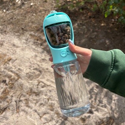 HydraBuddy drinkfles hond mintblauw — hand houdt complete fles buiten vast, snacks zichtbaar door transparant raam